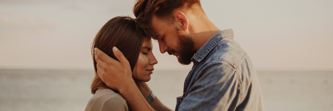 What It's Like to Have a Partner With Hypothyroidism man and woman standing in front of the ocean and touching foreheads