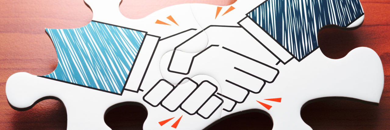 Hiring New Personal Care Assistants to Help With a Disability Handshake jigsaw puzzle pieces on wood desk.