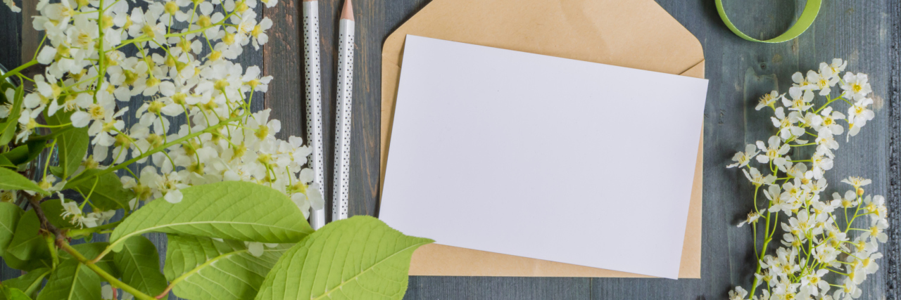white greeting card surrounded by white flowers and green leaves
