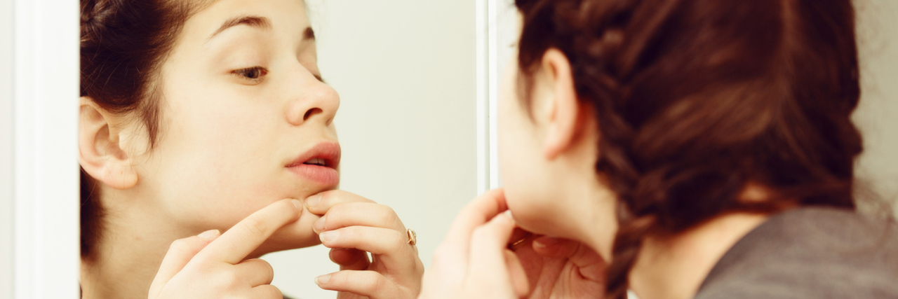 How I Discovered My Skin Picking Was Actually a Disorder young woman cleaning pores or picking skin in front of mirror