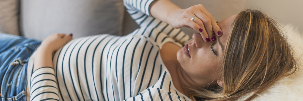 What We All Need to Realize About Post-Concussion Syndrome A woman laying on a couch with her hand to her head.