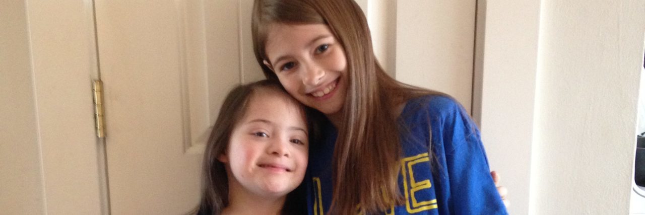 My Sister Has Down Syndrome and It's OK With Me Two sisters hugging. One with Down syndrome. They are weraing blue shirts that say, "Love doesn't count chromosomes"