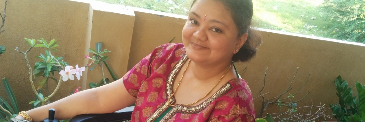When People Assume I'm Not Capable Because of My Disability Aarthi on her patio, wearing a red and green sari.