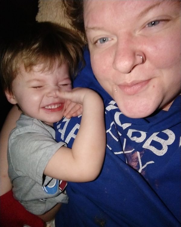 Mother and toddler son taking a selfie. Little boy is cuddled close to his mom as they smile at the camera.