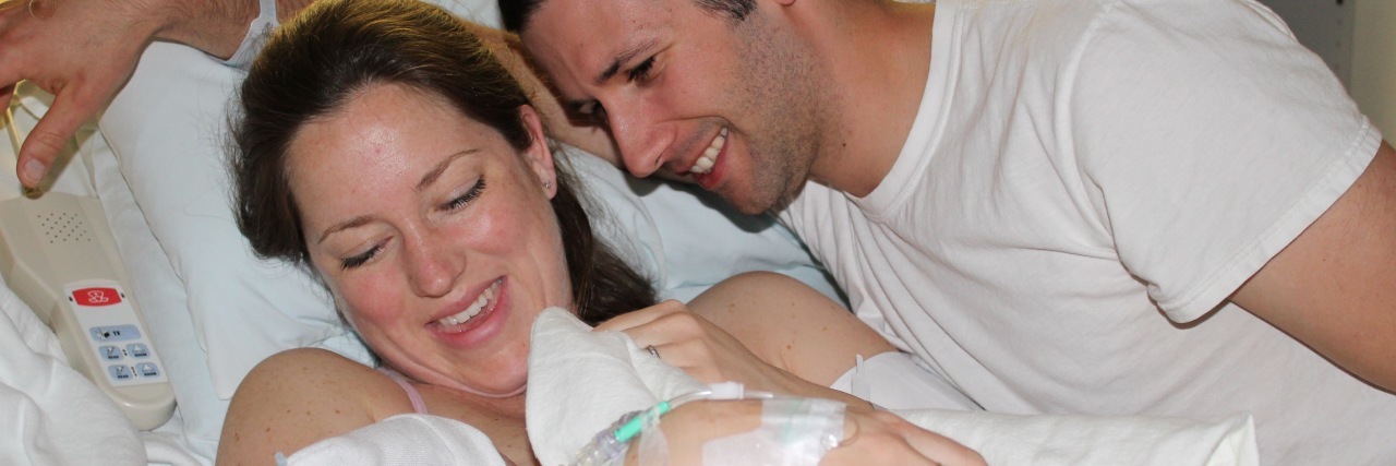 woman holding newborn baby in hospital bed with man smiling