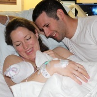 woman holding newborn baby in hospital bed with man smiling