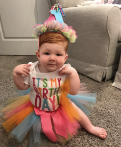 Red head baby on 1st birthday sitting on the floor with a colorful tutu and party hat