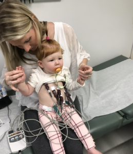 Baby girl siting on mom's lap and covered with wires to check her heart