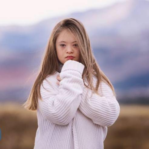 Image of kennedy Garcia posing, she wear a white fluffy sweater and she is resting her chin on her fist. Outdoor shot.