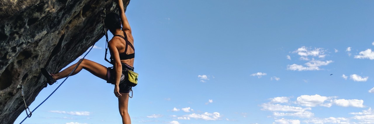 What Rock Climbing in the Aussie Outback Taught Me About My Anxiety young woman rock climbing on cliffside hanging on by one hand tropical location