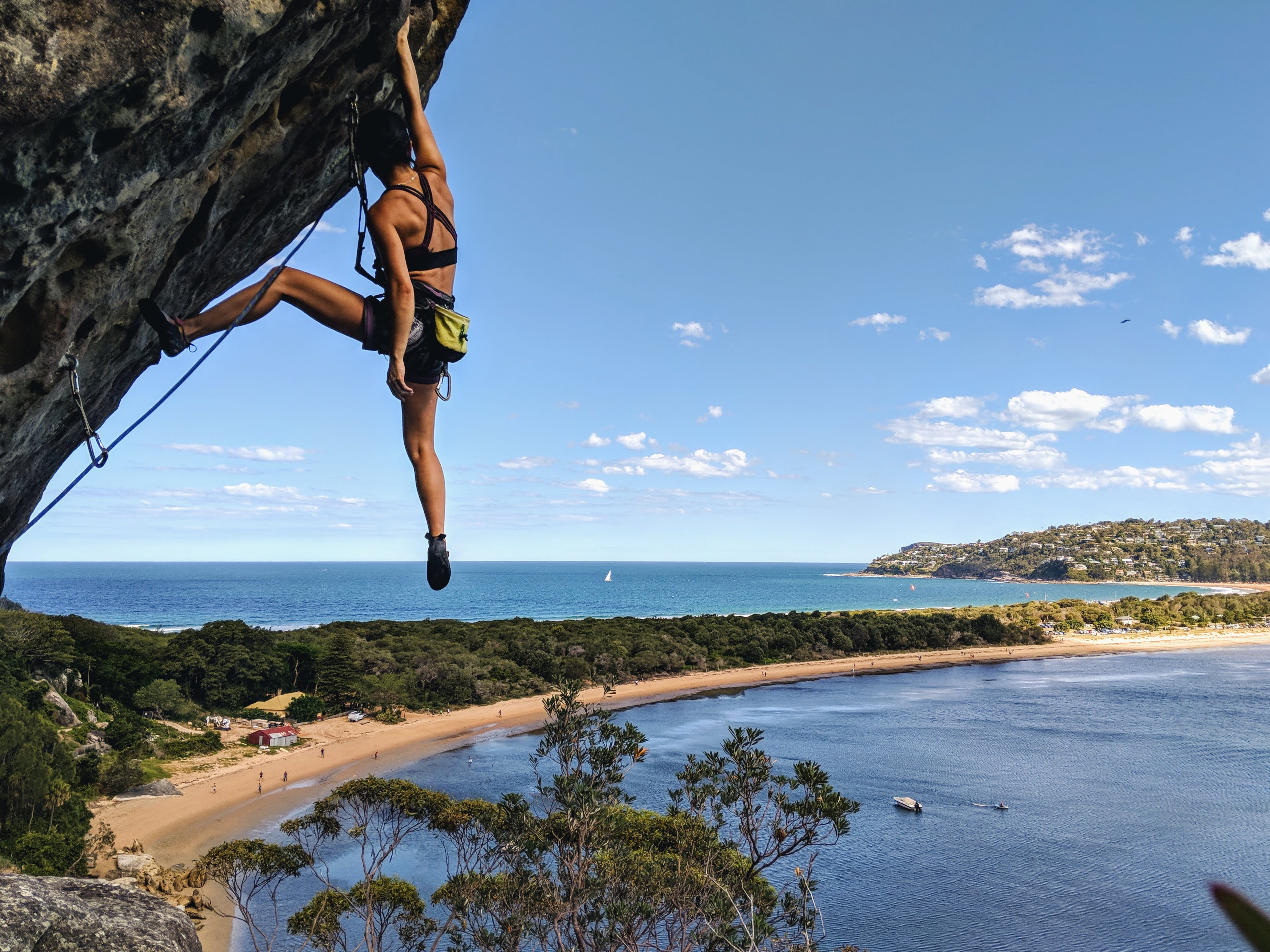 young woman rock climbing on cliffside hanging on by one hand tropical location