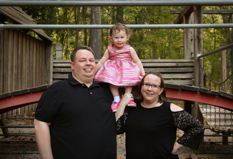 Melissa smiling with her daughter and husband in front of a house