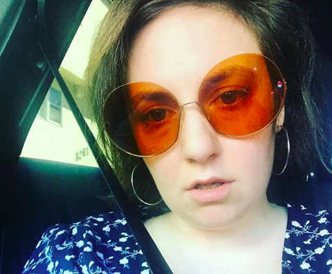 lena dunham taking a selfie wearing orange sunglasses and a blue shirt