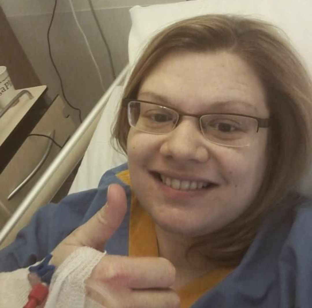 woman lying in a hospital bed and giving a thumbs up