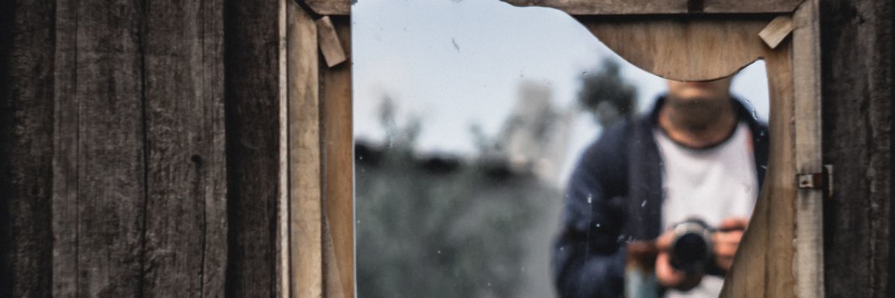 reflection of man in broken mirror with face obscured and camera in hands