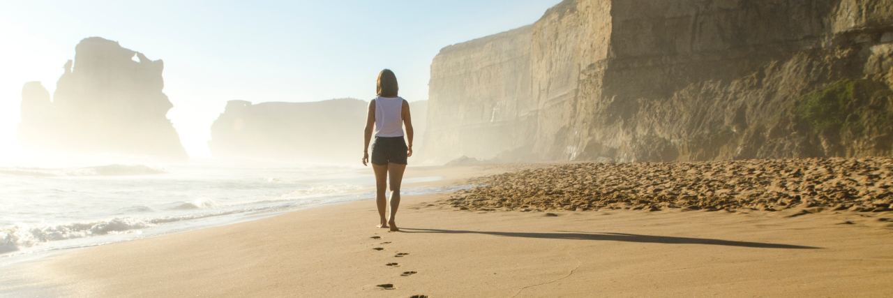 woman walking along a beach with a trail of footprints in the sand behind her
