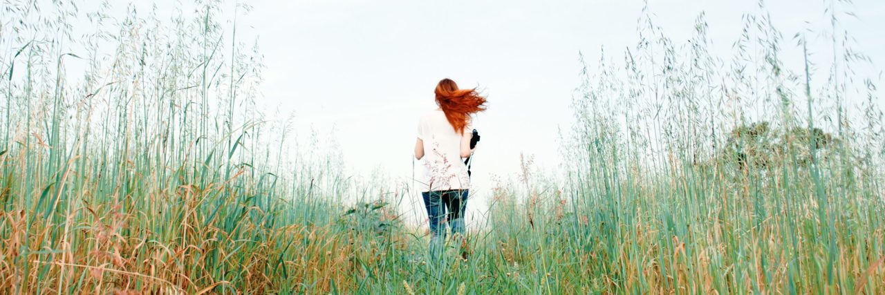 redhead woman running through long grass in field away from camera