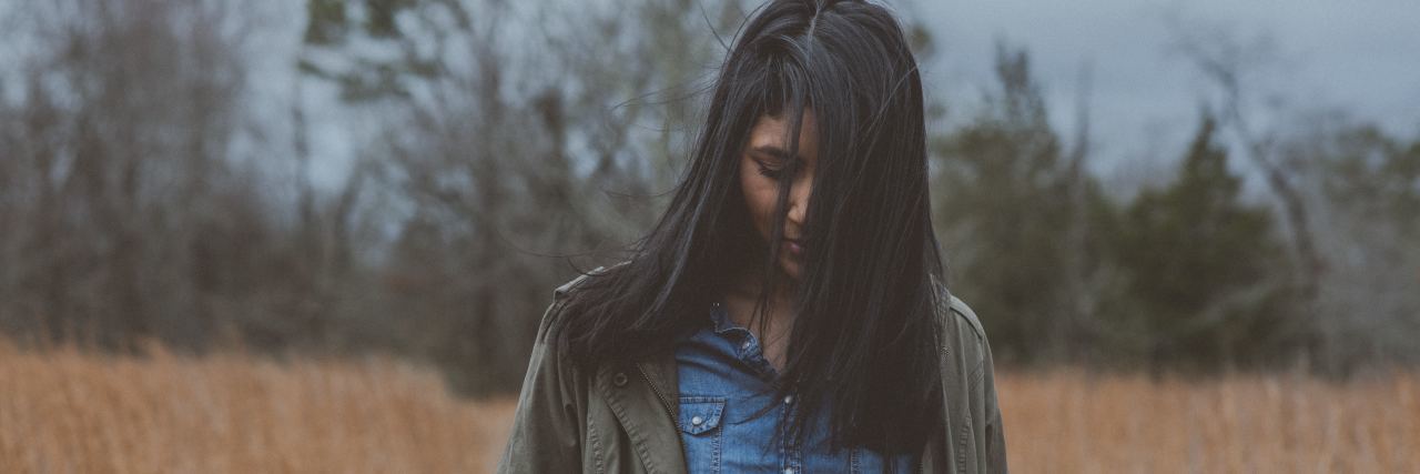 How I'm Surviving the Pain of My Mother's Death by Suicide woman in field looking down with her hair in front of her face
