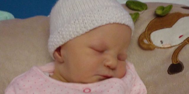 The author's daughter wearing a onesie that says "little sister"