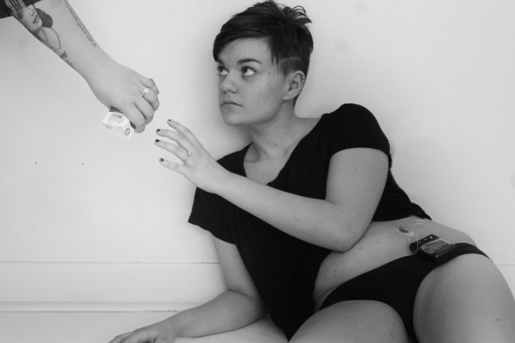 black and white photo of woman sitting on the ground with a tube in her stomach and reaching out to take something from a person's hand