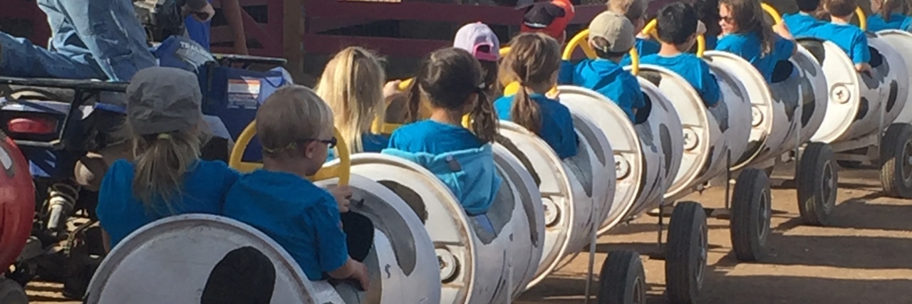 A Thank You to the Parents Raising Inclusive Kids Children wearing blue shorts riding a single car train at school event or fair. Back view, no faces visible.