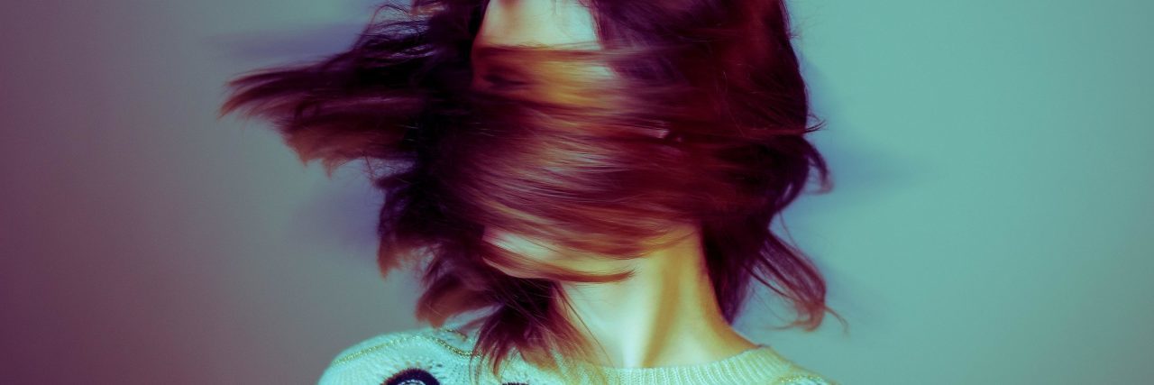 high contrast color blurred image of woman swinging hair covering face