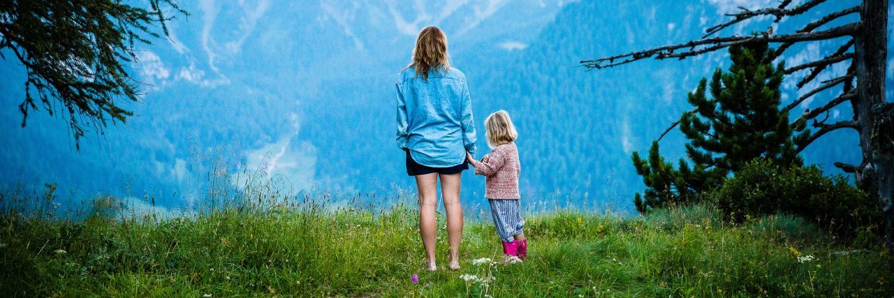 Mother and daughter standing together in clearing in front of mountains