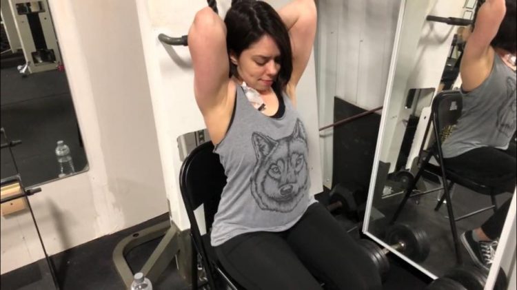 woman in a gray tank top and an IV in her chest lifting weights in the gym