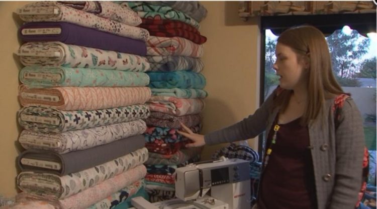 woman standing by her sewing machine and pointing to a stack of fabrics