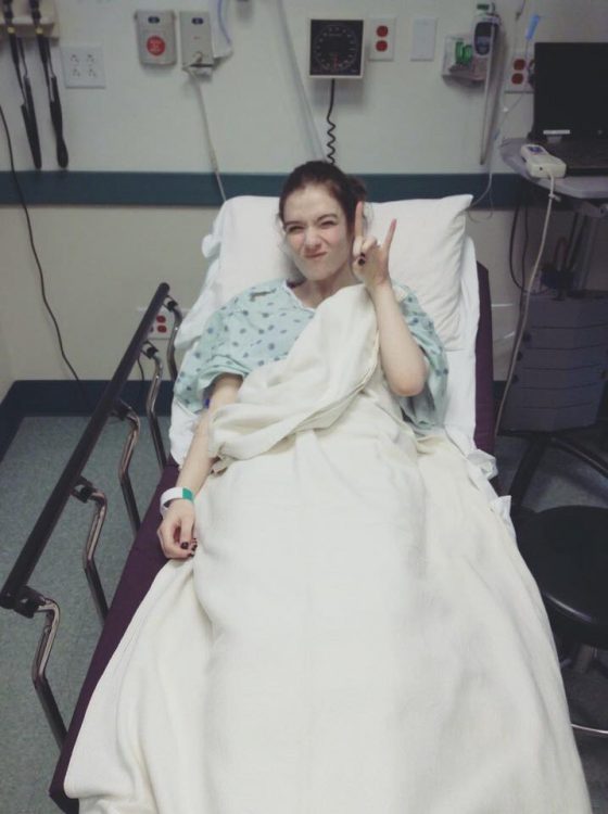 woman lying in a hospital bed and making the 'rock n roll' sign with her hand