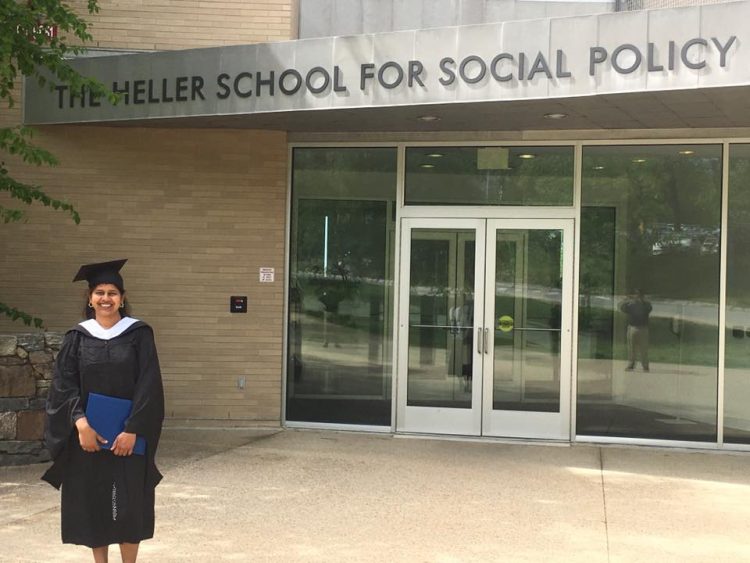 woman wearing a graduation cap and gown and holding a degree outside of her college