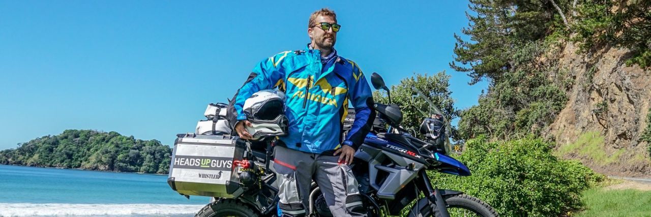 Colby Ellis posing in front of motorcycle while circumnavigating the world for mental health awareness with HeadsUpGuys