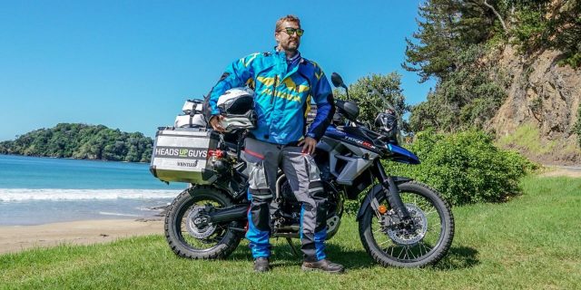 Colby Ellis posing in front of motorcycle while circumnavigating the world for mental health awareness with HeadsUpGuys