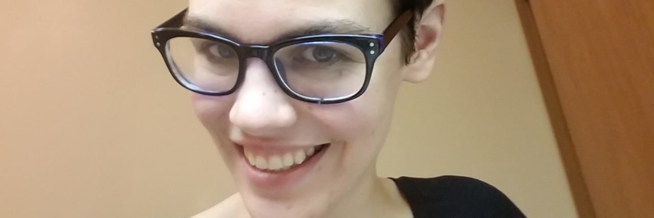 The Importance of Getting to Know Yourself When You're Chronically Ill selfie of the author. she is smiling and wearing a black shirt and glasses.