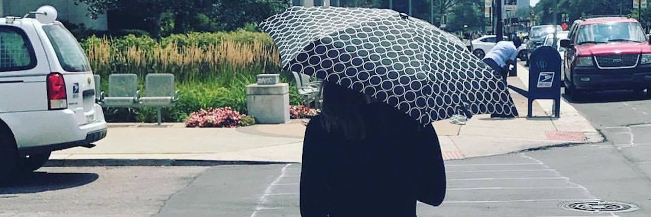 When We Realized My Body Doesn't Love the Sun A picture of the writer walking down the street with an umbrella and in long sleeves.