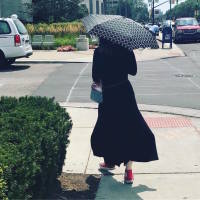 A picture of the writer walking down the street with an umbrella and in long sleeves.
