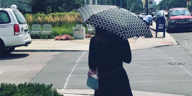 A picture of the writer walking down the street with an umbrella and in long sleeves.