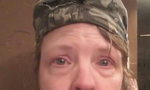 close-up photo of a woman's face. she's wearing a green camo hat and is crying