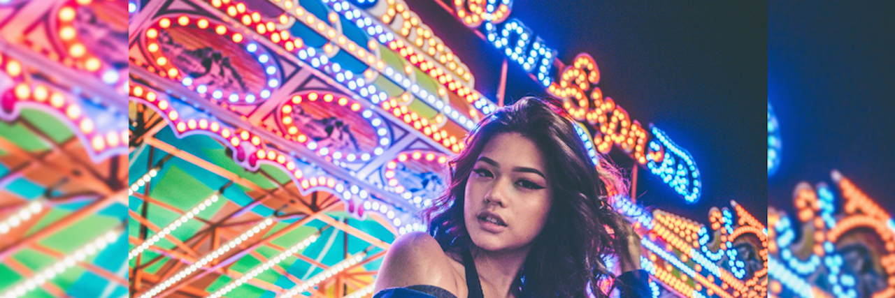 29 Ways People With Borderline Personality Disorder Self-Sabotage A woman beneath carnival lights, juxtaposing her casual demeanor with the chaotic lighting. 29 Ways People With Borderline Personality Disorder Self-Sabotage.