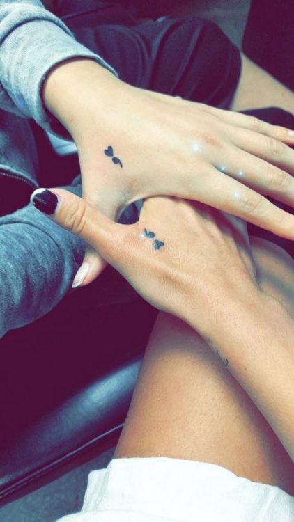 two people handing hands with semicolon tattoos 