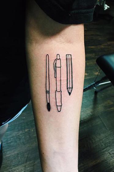 A tattoo of a paintbrush, a pen and a pencil
