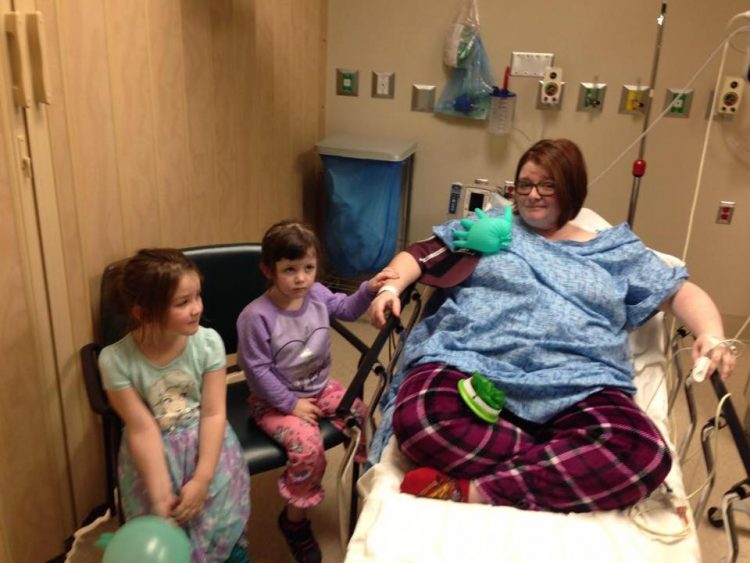 woman sitting on hospital bed with two young kids on chairs next to her