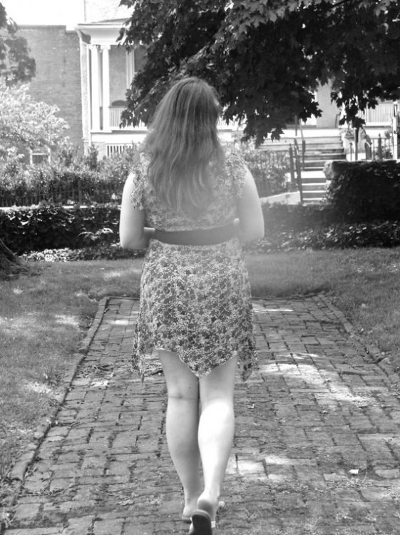 black and white photo of a woman in a dress walking outside