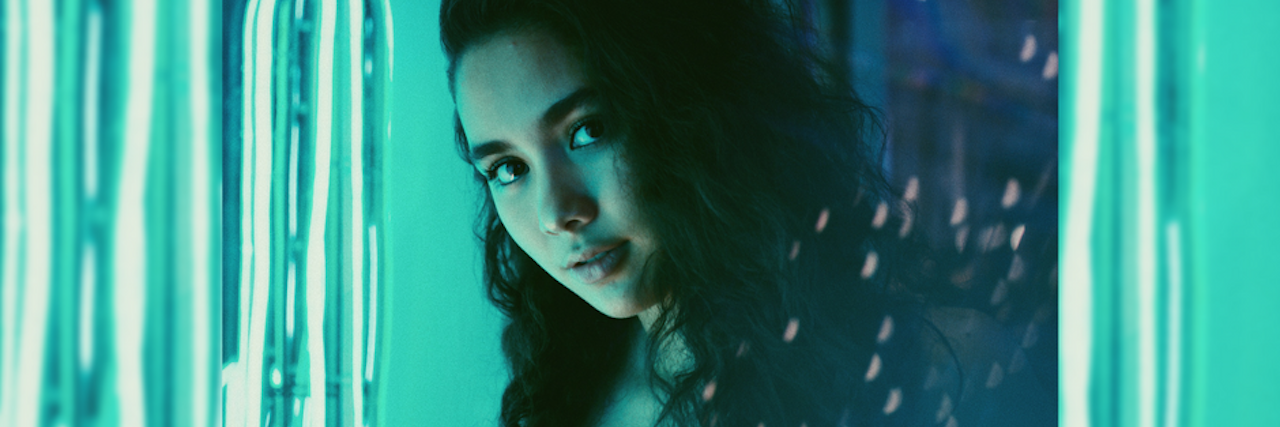 A young woman at a neon-lit party looks directly at the camera. 5 Things People With Borderline Personality Disorder Do That Get Mistaken for 'Manipulation'