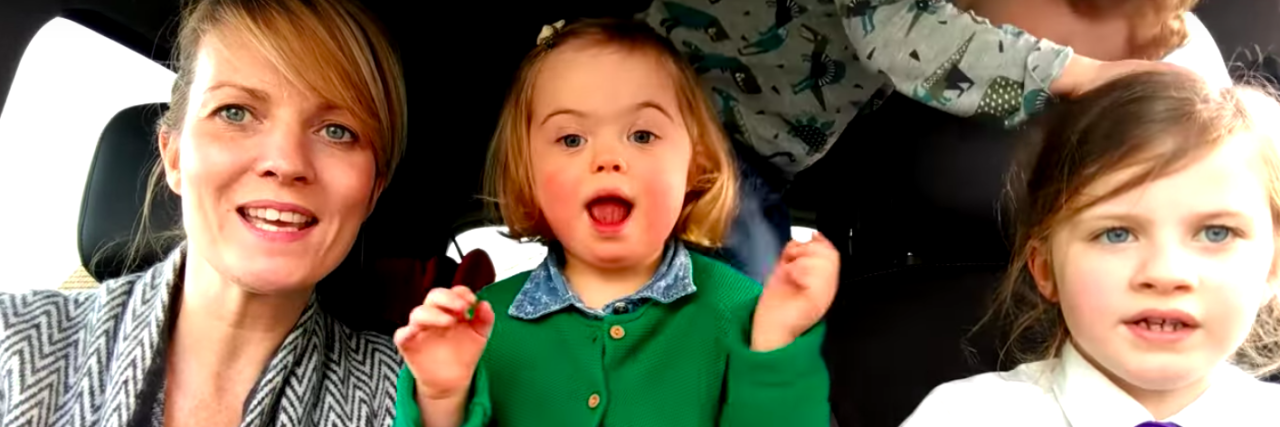 Screen shot of little girl with Down syndrome in car with mom and two siblings singing