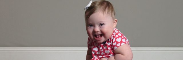 Baby girl with Down syndrome sitting on floor smiling at camera