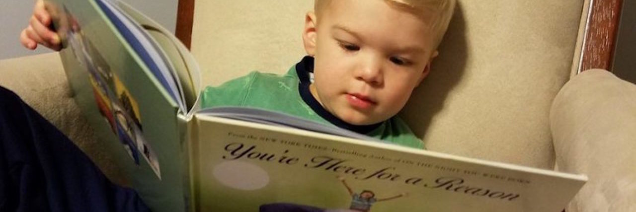What the Book 'You Are Here for a Reason' Means as a CHD Parent young boy sitting in an armchair holding a book