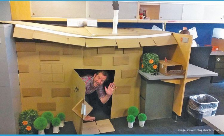 a man's office desk transformed into a tiny house and him peeking out the door and waving