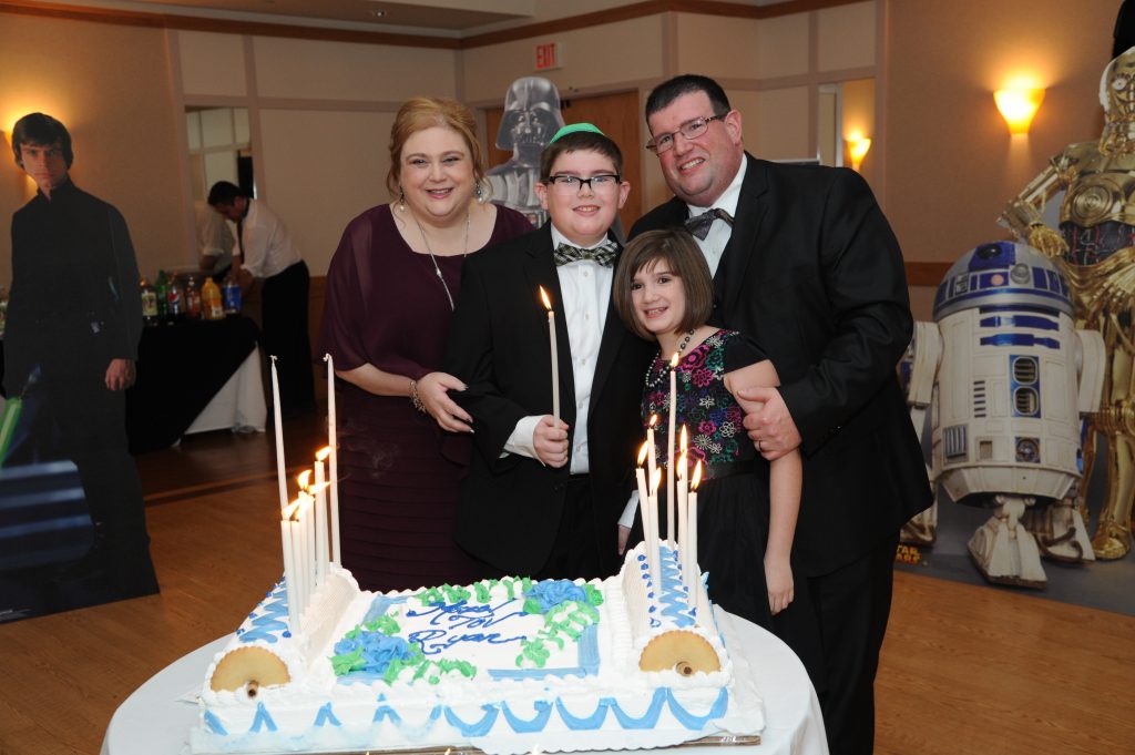 mother, father, daughter and son at the son's bar mitzvah standing in front of a cake