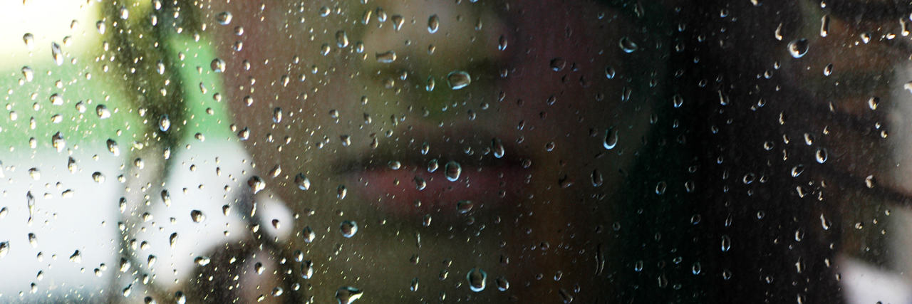 Feeling Trapped in Your Body Due to Fibromyalgia woman standing in front of the window while it's raining